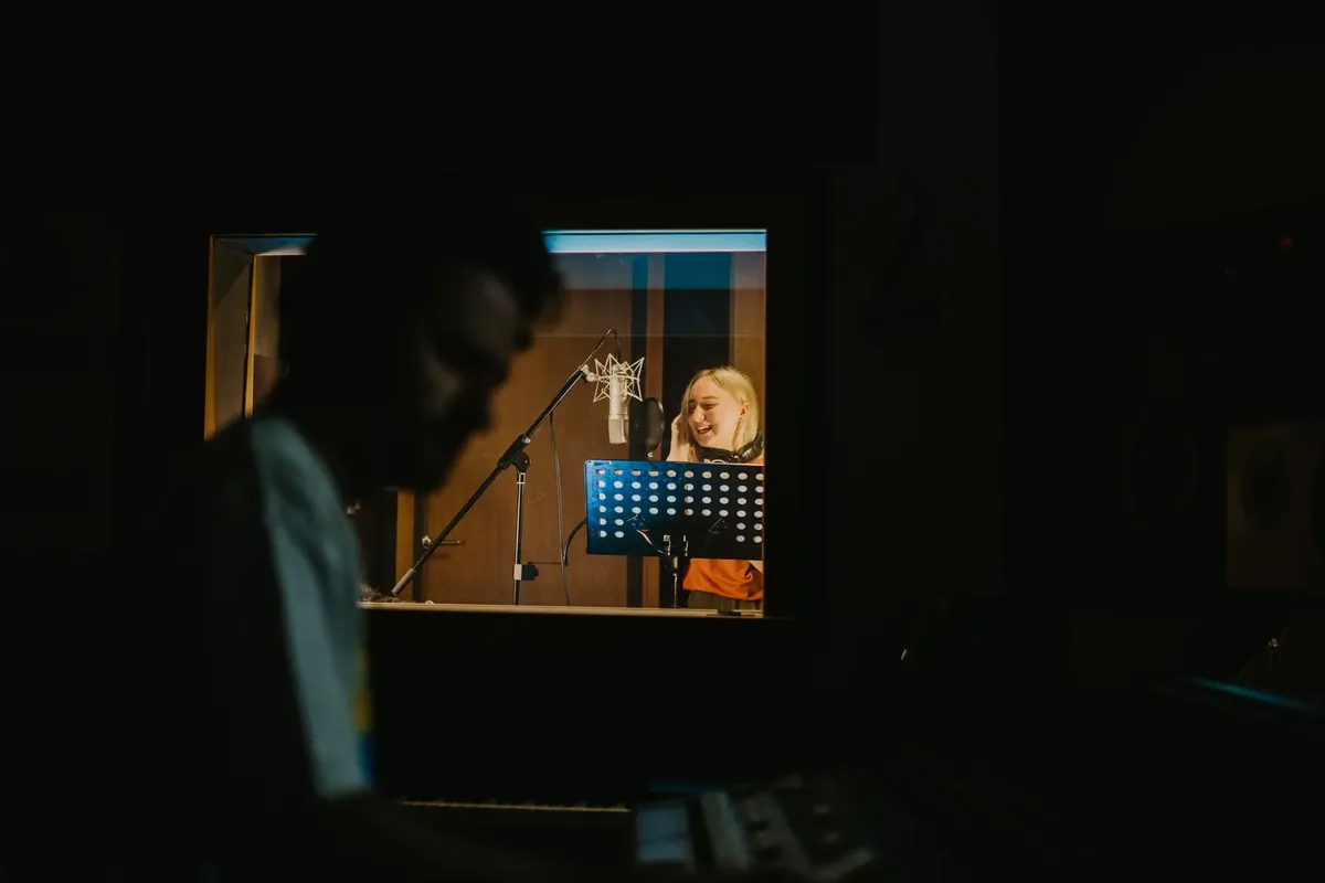 Female singer performing in a dimly lit music studio recording her voice behind a microphone.