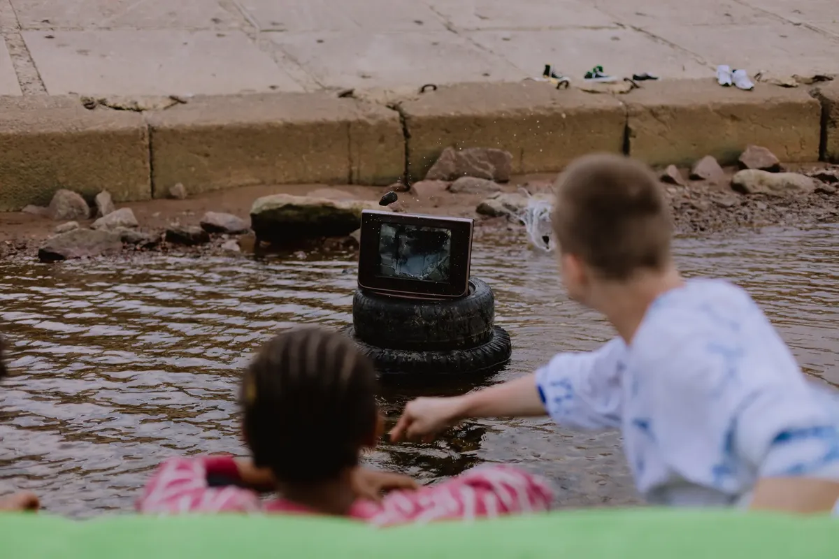 Teenagers watching a broken TV in water, creating a unique scene of urban exploration.