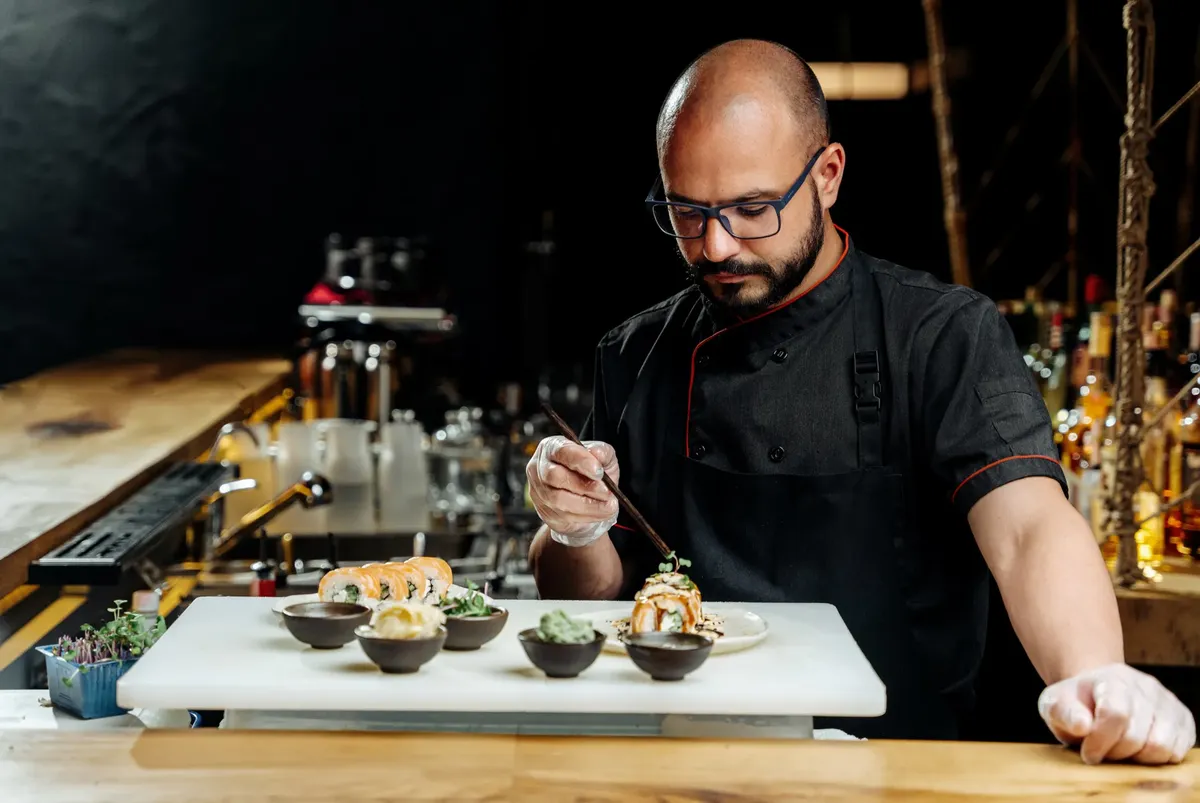 Skilled chef meticulously preparing sushi rolls in a modern kitchen setting, focusing on food presentation.