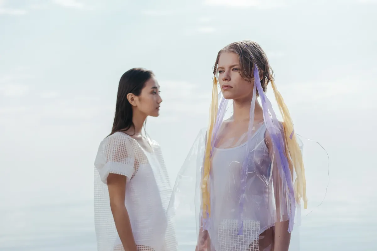 Two women in artistic fashion posing near the seaside, showcasing modern style.