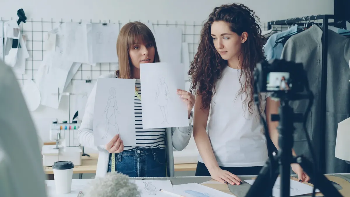 Two fashion designers showcasing sketches in a creative studio setting.