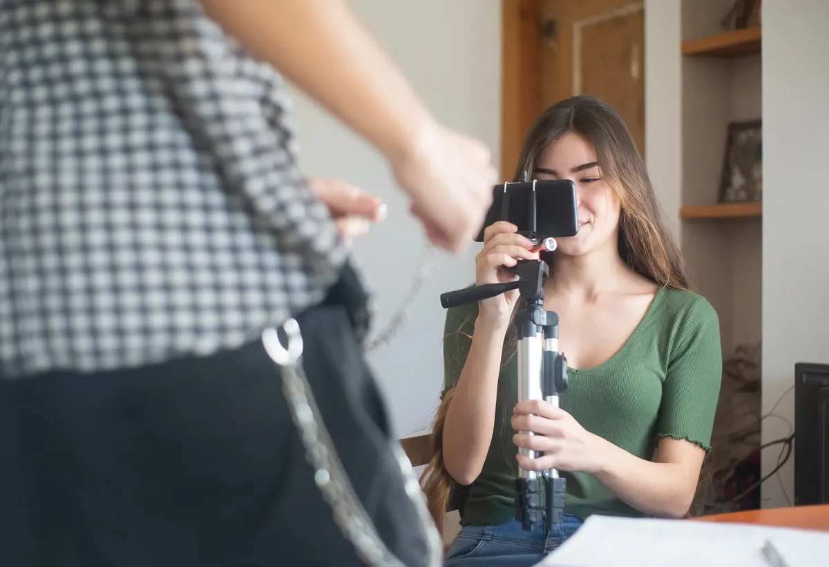A young woman vlogs indoors using a smartphone mounted on a tripod, capturing content creation.