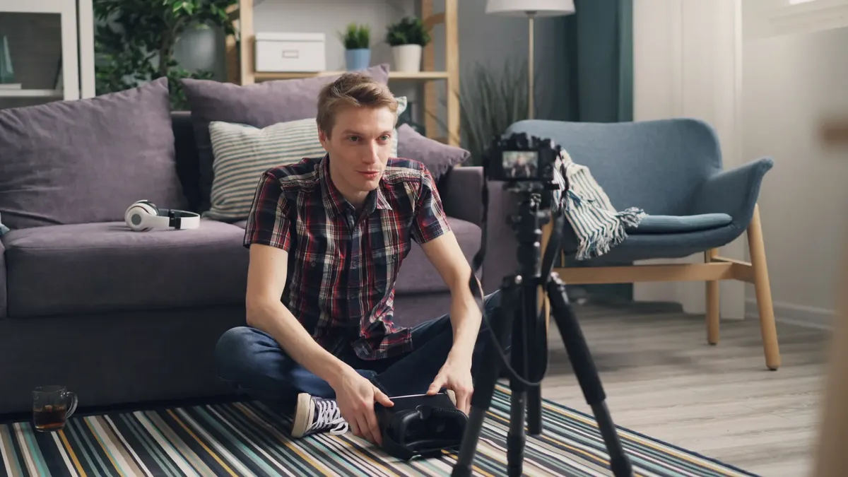 Young man sitting on the floor filming a vlog in a cozy living room with camera and tripod.