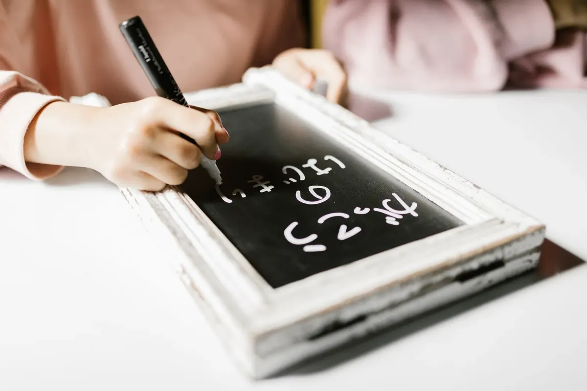 Child writing on a small chalkboard, exploring creativity and education indoors.